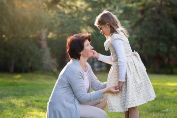 Happy mother and little daughter looking at each other, little girl holding mother's cheek, mother's day concept