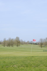 Obraz premium A red and white checkered golf course flagstick on a putting green.
