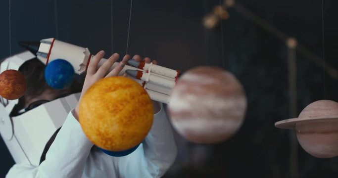 CU Cute little boy wearing cardboard astronaut helmet flying toy rocket through planets, exploring deep space. 4K UHD 60 FPS SLOW MO