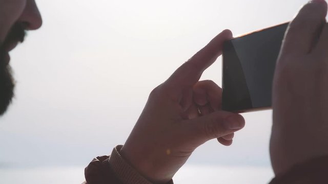 POV. A man with a beard and wearing glasses takes off on a smartphone on a sunny day. Hicker man taking a photo of winter nature. The tourist admires nature and makes photos.