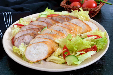 Juicy home made sausage with a light spring salad of fresh vegetables on a black wooden background. A traditional Easter dish.