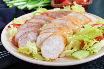 Juicy home made sausage with a light spring salad of fresh vegetables on a black wooden background. A traditional Easter dish.
