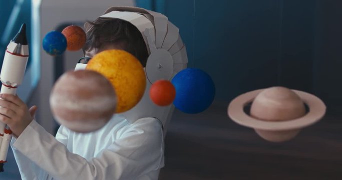 CU Cute little boy wearing cardboard astronaut helmet flying toy rocket through planets, exploring deep space. 4K UHD 60 FPS SLOW MO