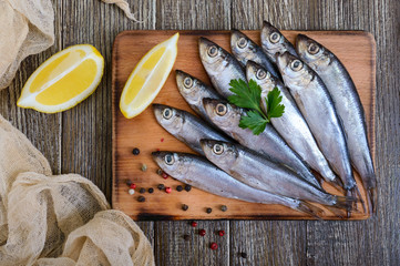 A small salted hamsa (sprat) with spices, lemon on a wooden background. Top view.
