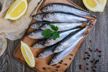 A small salted hamsa (sprat) with spices, lemon on a wooden background. Top view.