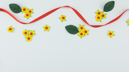 Yellow paper flowers and green leaves with red ribbon on white background with copy space