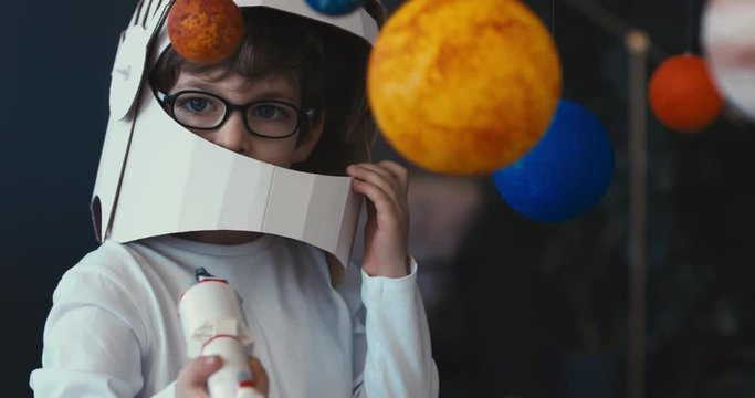 CU Cute little boy wearing cardboard astronaut helmet flying toy rocket through planets, exploring deep space. 4K UHD 60 FPS SLOW MO