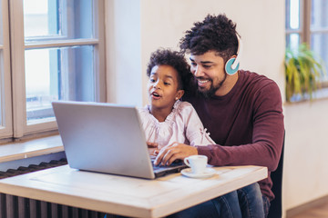 Young black father siting together with his daughter, they are using a laptop.