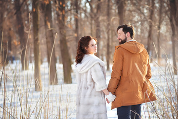 A wedding couple in winter clothes hold hands and stroll through the park on a sunny winter day.