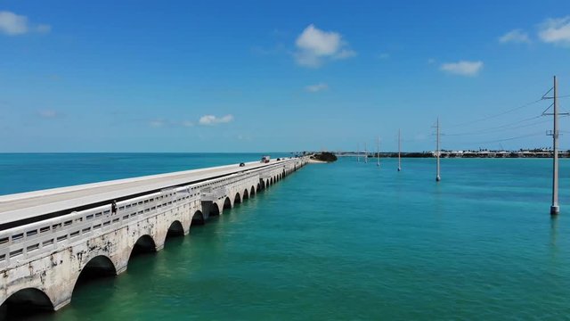 Aerial view of a highway and bridge connecting the Florida Keys. Fisherman and traffic on the bridge. Sunny day with warm blue water. The clip focuses on the side view of the bridge. 