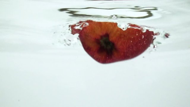 Slow motion of falling fresh red apple into water. 4K