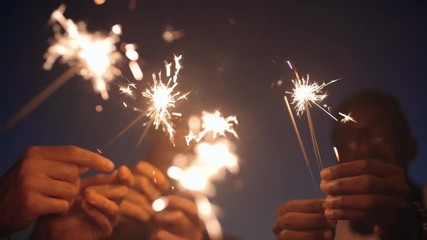 Close up of happy people lighting sparklers and dancing at night - Powered by Adobe