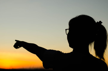 The silhouette of a woman standing pointing forward at sunset.