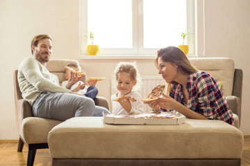 Parents with children eating pizza together and having fun in living room
