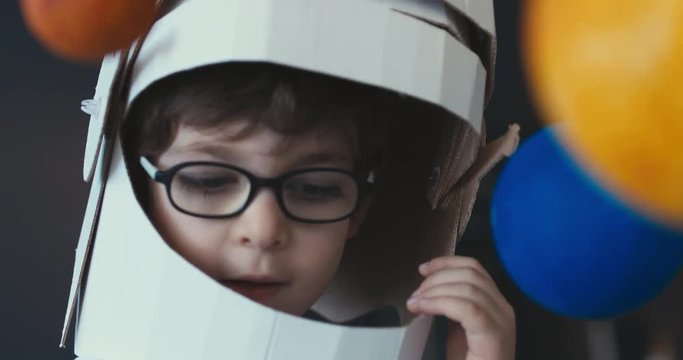 CU Cute little boy wearing cardboard astronaut helmet flying toy rocket through planets, exploring deep space. 4K UHD 60 FPS SLOW MO