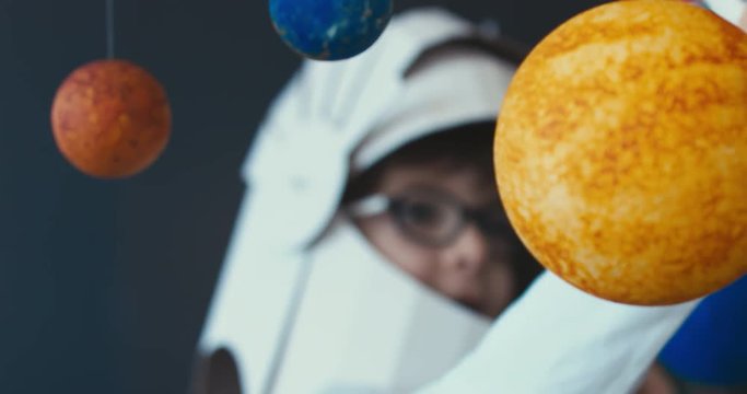 CU Cute little boy wearing cardboard astronaut helmet flying toy rocket through planets, exploring deep space. 4K UHD 60 FPS SLOW MO