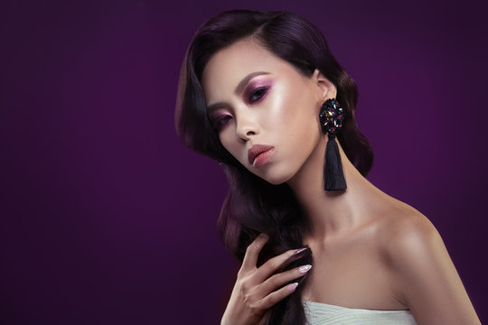 Fashion beauty portrait of a chic girl of Asian appearance with an elegant wave arrangement on a purple background.