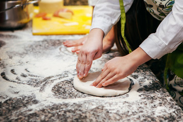 cook shows children how to roll out the dough for pizza