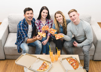 The four happy people on the sofa eating pizza