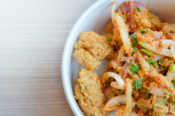 Spicy chicken with rice in bowl on wood background.