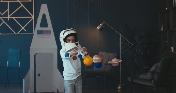 WIDE Cute little boy wearing cardboard astronaut helmet flying toy rocket through planets, exploring deep space. 4K UHD 60 FPS SLOW MO