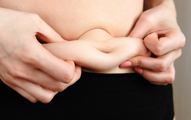 Thin young woman examines the folds on her stomach standing in front of a mirror in her underwear. Belly and arms close up