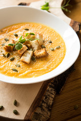 White bowl with pumpkin soup and bread chunks