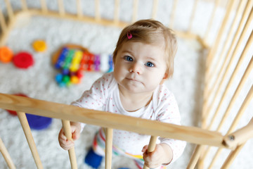 Beautiful little baby girl standing inside playpen. Cute adorable child playing with colorful toy