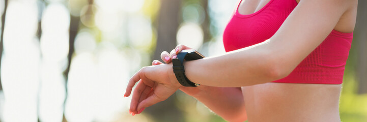 Attractive female athlete using fitness app on her smart watch to monitor workout performance. Web banner.