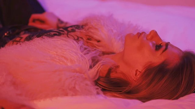 Tired girl showing middle finger. Young woman wearing fur jacket and resting in bed