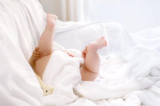 Cute little baby playing with own feet after taking bath. Adorable beautiful girl wrapped in white towels
