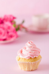 Cupcake with pink cream decoration and roses on pink pastel background.