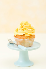 Cupcake with yellow cream decoration on blue stand on yellow background - pastel vertical banner. Minimalism still life concept.