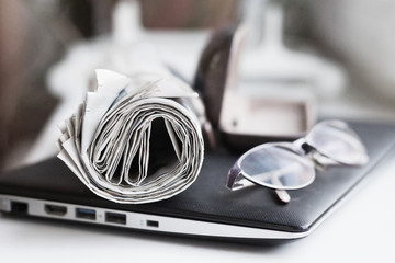 Laptop, newspapers and glasses on the desk in office, side view