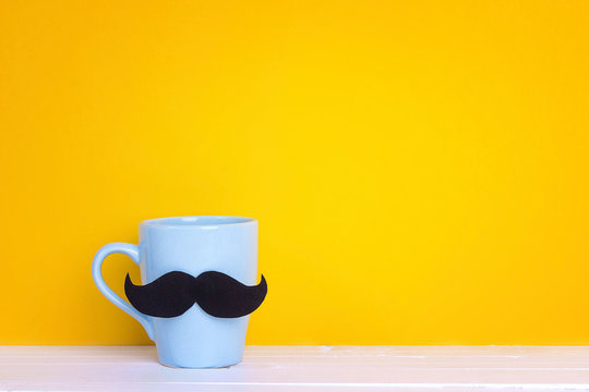 Blue mug with a mustache on yellow background. Copy space. Fathers day holiday.