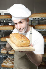 Piekarnia. Przystojny piekarz z bochenkiem świeżego chleba stoi w piekarni.




