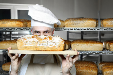 Żytni chleb. Przystojny piekarz z bochenkiem świeżego chleba stoi w piekarni.
