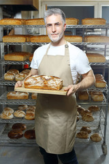 Piekarz. Przystojny piekarz z bochenkiem świeżego chleba stoi w piekarni. - obrazy, fototapety, plakaty
