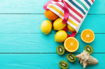 Summer fun time and fruits on blue wooden background. Mock up and picturesque. Orange, lemon, kiwi fruit in bag and shell on the table.