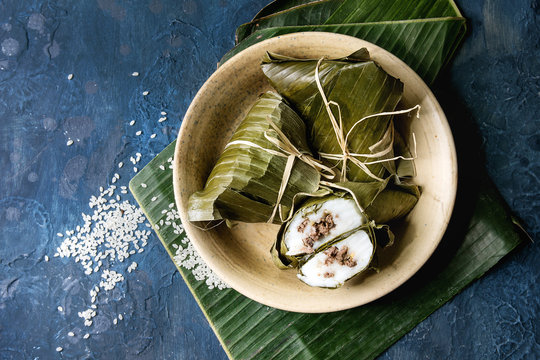 Asian rice piramidal steamed dumplings from rice tapioca flour with meat filling in banana leaves served in ceramic bowl with rice above over blue texture background. Top view, space.
