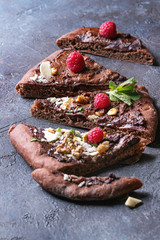 Sliced homemade sweet dessert chocolate pizza with different chocolates, raspberries and mint served with ingredients above over blue texture background.