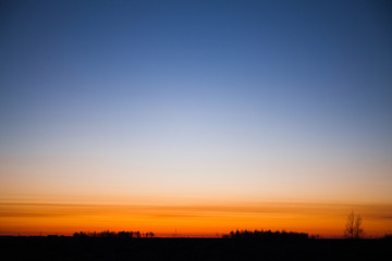 Bright red dawn with a cloudless blue sky. Silhouette of the earth and trees. Copy space for text.