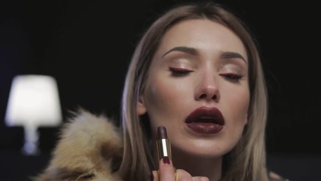 Girl paints lips with lipstick on dark background. Beauty lips make-up. Fashion makeup.
