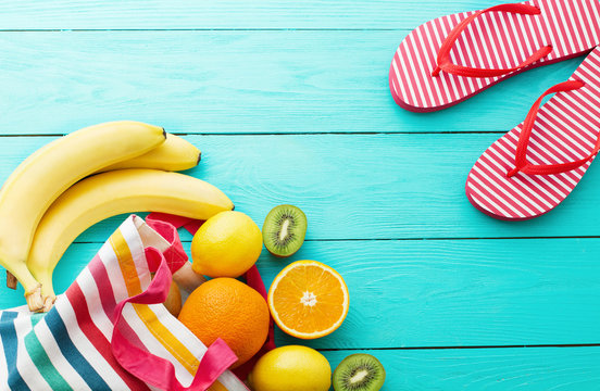 Summer fun time. Fruits on blue wooden background. Orange, lemon, kiwi, banana fruit in bag and flip flops on the floor. Top view and copy space