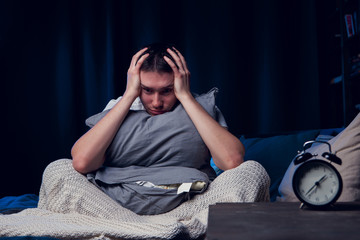Photo of man with insomnia with pillow sitting next to alarm © Sergey Mironov