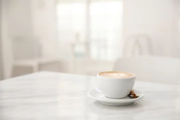 Keuken spatwand met foto Cappuccino coffee cup on white marble table © Oran Tantapakul