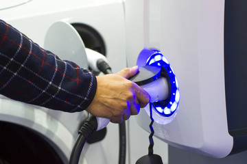 Human hand is holding Electric Car Charging nozzle. Selective focus on hand and nozzle