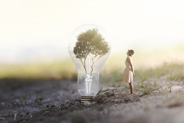 surreal image of a woman who observes intrigued a giant bulb containing a tree for renewable energy - obrazy, fototapety, plakaty