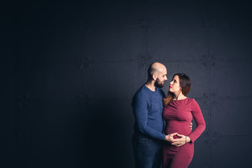 bearded man holding belly of pregnant woman in studio on dark background. Copy space.