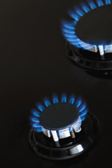 Two gas burners are burning with blue gas on the dark stove. Closeup, selective focus